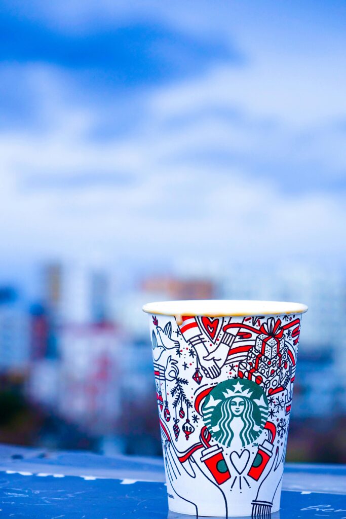 Christmas themed Starbucks hot cup on a ledge with a blurry background.